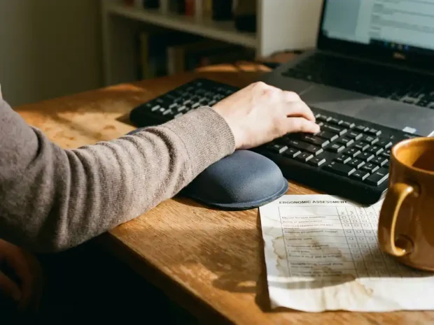 Polssteunbrace naast een toetsenbord op een houten thuiswerkbureau, met een ergonomische checklist half onder een koffiemok.